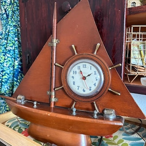 May include: A wooden sailboat clock with a white face and black numbers. The clock is on a tray with a floral pattern.