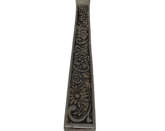 Puede incluir: Un cuchillo de mantequilla plateado con un diseño floral grabado en el mango. El mango es rectangular con un patrón detallado de flores y hojas. La hoja es lisa y redondeada.