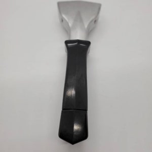 May include: A silver-colored spatula with a black handle. The spatula head is rectangular with a pointed tip. The handle is a solid black color and has a geometric shape.