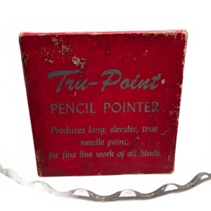 May include: A red rectangular box for a Tru-Point pencil pointer. The front features the text: Tru-Point PENCIL POINTER, Produces long, slender, true needle point, for fine line work of all kinds. The box shows signs of wear on the edges.