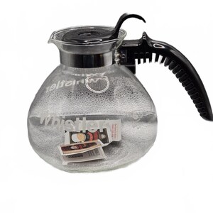 Könnte beinhalten: Eine Kaffeekanne aus klarem Glas mit einem schwarzen Kunststoffgriff und Deckel. Das Wort Whistler ist in Weiß auf die Vorderseite des Glaskörpers gedruckt. Ein kleines Papieretikett mit Produktbildern ist vorne an der Kanne befestigt.