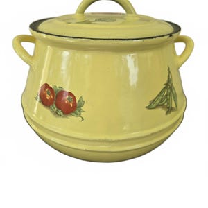 May include: A pale yellow enamel pot with a matching lid and two side handles. The exterior features a decorative print of two red tomatoes with green leaves on the left and a cluster of green pea pods on the right side of the rounded body.