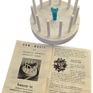 Pode incluir: Um fabricante de laços de plástico branco vintage com uma peça central azul e pinos. O manual de instruções está aberto, mostrando um diagrama de um laço e o texto "Bow Magic".