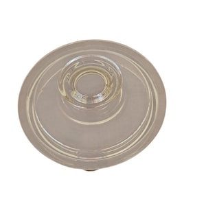 May include: Clear glass lid with a circular design. The lid has a central knob and a wide, flat rim. The glass appears to be smooth and transparent, suitable for a jar or container.