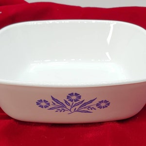 May include: White, square casserole dish with two handles and a floral design in purple. The dish is made of a durable material and is suitable for baking and serving. A classic piece for any kitchen.