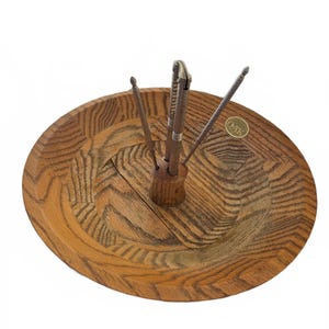 May include: A wooden nut bowl with a central holder containing nutcrackers and picks. The bowl is round with a textured, light brown finish. The nutcracker is silver and the picks are metal. A small "OAK" sticker is visible.