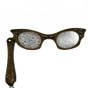 Op de afbeelding: Een lorgnet in vintage-stijl met een donker olijfgroen montuur versierd met strass-steentjes. De glazen hebben een textuur met een waterdruppelpatroon. Een enkele scharnierende handgreep aan de linkerkant is eveneens versierd met steentjes.