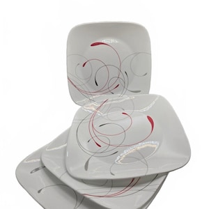 May include: A set of three white square plates stacked on top of each other. Each plate features a decorative pattern of thin, flowing lines in black, grey, and red that swirl across the surface, creating a dynamic and abstract visual design.