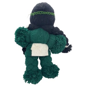 May include: A green yarn doll with black yarn hair and a white fabric apron. The doll has pom-poms for arms and legs.