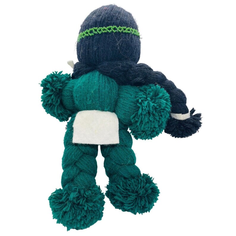 May include: A handmade yarn doll with a green body, black hair, and a white fabric patch. The doll has pom-poms for arms and legs.
