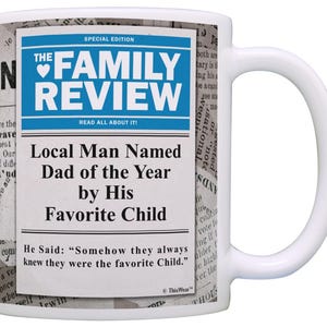 May include: White ceramic mug with a newspaper-style design. The mug features the headline "THE FAMILY REVIEW" in blue and white, with the text "Local Man Named Dad of the Year by His Favorite Child."
