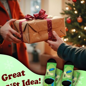 May include: A wrapped gift box with a burgundy ribbon is being passed between two people. The image also features green socks with a disc golf course design and the text "Great Gift Idea!"