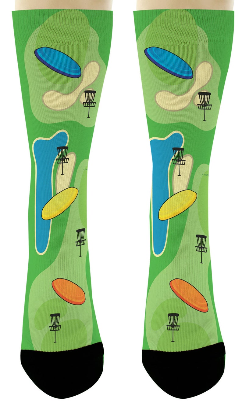 May include: Green socks with a disc golf course design. The socks feature a repeating pattern of disc golf baskets, discs, and water hazards. The socks have black toes and heels.