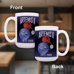 May include: White ceramic mug featuring the text "ARTEMIS II" above illustrations of Mars, Earth, and the Moon. The mug also displays the years "1972-2026" and has a large, curved handle. The mug is a space exploration theme.