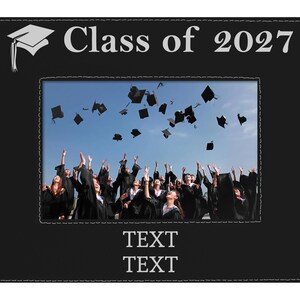 May include: A black rectangular picture frame with white stitching along the edges. The top features a white graduation cap icon and the text "Class of 2027". The center holds a photo of graduates throwing caps. The bottom has two lines of "TEXT".