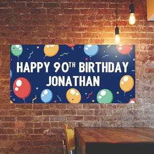 May include: A navy blue banner with the text "HAPPY 90TH BIRTHDAY JONATHAN" in white. The banner is decorated with colorful balloons in red, blue, yellow, and green, with confetti and wavy lines.