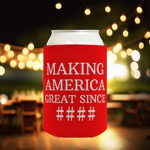 May include: Red can cooler with white text that reads "Making America Great Since # # # # #".
