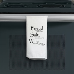 May include: White kitchen towel with black text that reads "Bread so you never know hunger, Salt so your life always has spice, Wine so joy and vitality live forever".