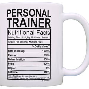May include: White ceramic coffee mug with a black graphic that reads "Personal Trainer" and a nutritional facts table listing "Hard Working", "Passion", "Determination", "Pride", "Regret", and "Caffeine" with percentage values.