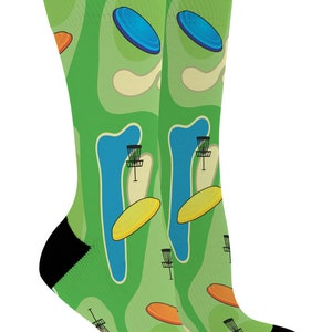 May include: A pair of green socks with a disc golf course design. The socks feature a repeating pattern of blue and orange flying discs, baskets, and a course layout. The heels and toes are black.