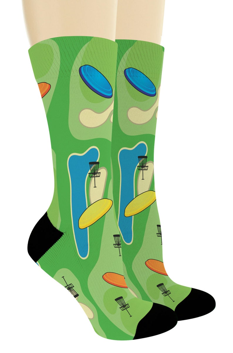 May include: A pair of green socks with a disc golf course design. The socks feature a repeating pattern of blue and orange flying discs, baskets, and a course layout. The heels and toes are black.