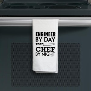 May include: White kitchen towel with black text that reads "Engineer by Day Chef by Night" with a knife graphic.