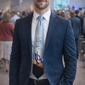 May include: A light blue tie with the text "For God so loved the world that He gave His only Son" and a cross graphic. The tie is worn with a navy blue suit and a white dress shirt.