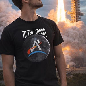 May include: Black t-shirt with the text "TO THE MOON" above a graphic of a moon with a rocket and the letter "A". The background shows a rocket launch with flames and smoke.