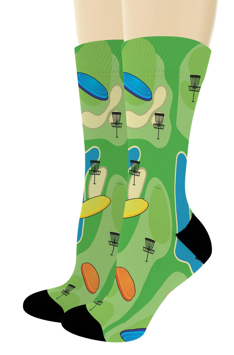 May include: A pair of knee-high socks featuring a vibrant green disc golf course design. The socks display a repeating pattern of disc golf baskets, discs, and course elements in shades of green, blue, yellow, and orange, with black heels and toes.