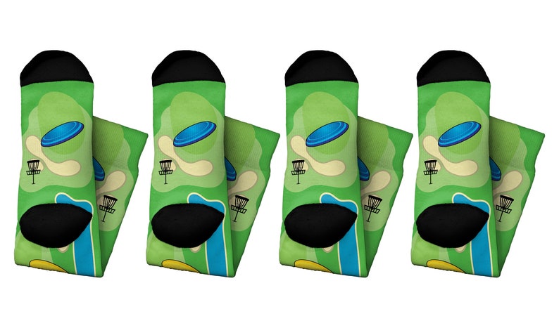 May include: Four pairs of socks with a green background featuring a blue disc flying over a disc golf course. The socks have black heels and toes, and the design includes a basket and a tee area.
