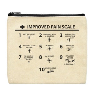 May include: A beige canvas zippered pouch with a black zipper. The pouch has a black and white graphic of a pain scale with a humorous take on pain levels. The text on the pouch reads "Improved Pain Scale" and includes phrases like "Why am I here?" and "Mauled by Wolves".