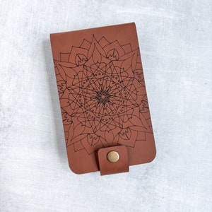May include: A brown leather wallet with a black mandala design and a brown button closure.