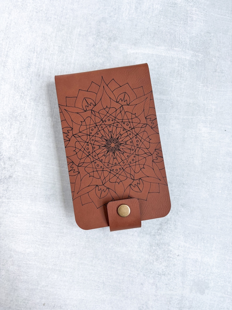 May include: A brown leather wallet with a black mandala design and a brown button closure.