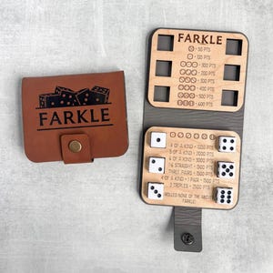 May include: A brown leather Farkle dice game set with a snap closure, featuring the game's name and dice illustrations. The open game board displays wooden dice and scoring information. The game is designed for multiple players.