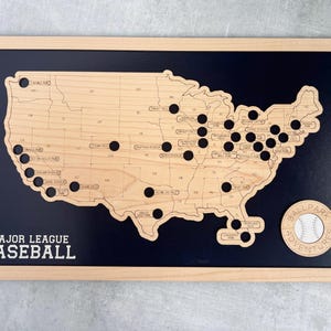 May include: Wooden Major League Baseball map with black dots marking locations. The map is framed in light wood and features the text "Major League Baseball" at the bottom. A circular emblem with a baseball and the words "Ball Park Adventures" is on the right.