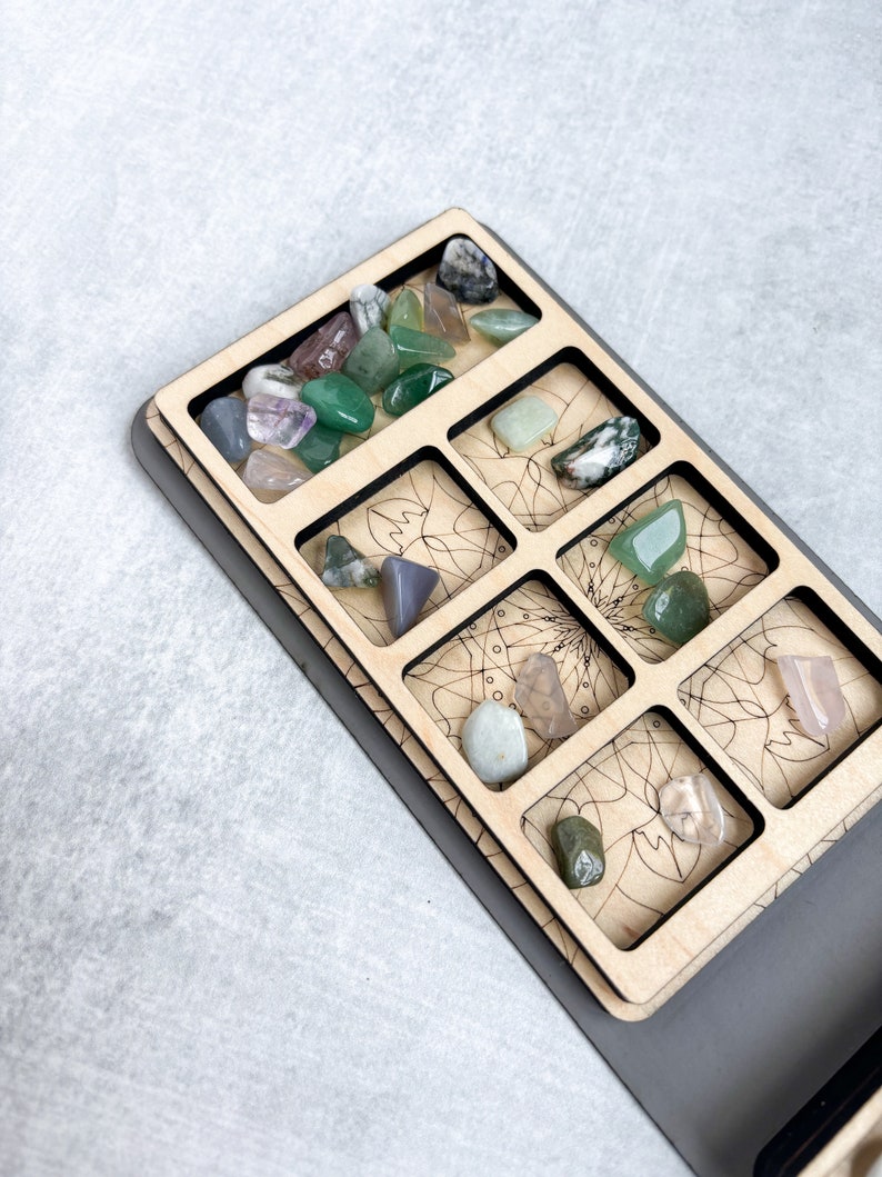 May include: A wooden tray with nine compartments, each containing a different type of stone. The stones are various shades of green, pink, and gray. The tray is decorated with a mandala design.