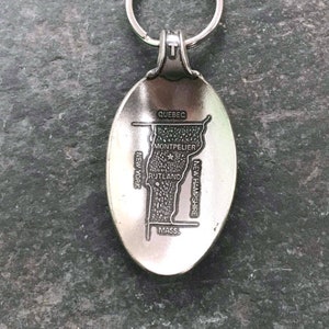 May include: Silver-colored keychain featuring an oval pendant with a detailed map of Vermont. The map includes the state's borders, major cities like Montpelier and Rutland, and neighboring states and Quebec. A key ring is attached at the top.
