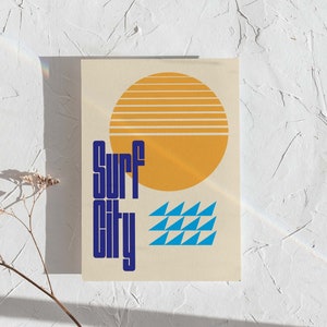 Puede incluir: Una tarjeta beige con un dise&ntilde;o gr&aacute;fico azul y amarillo. El gr&aacute;fico presenta un sol amarillo con rayas naranjas, un patr&oacute;n de olas azul y el texto "Surf City" en azul.