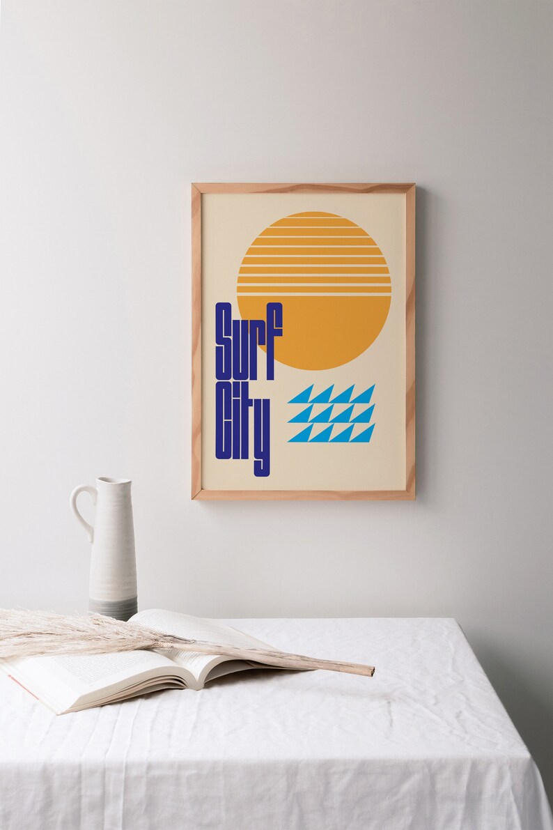 Puede incluir: Una impresi&oacute;n enmarcada con un dise&ntilde;o retro que presenta un sol amarillo con rayas naranjas, olas azules y el texto "Surf City" en azul.