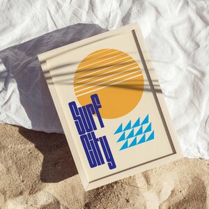 Puede incluir: Una impresi&oacute;n enmarcada con un dise&ntilde;o retro que presenta un sol amarillo con rayas azules y blancas, tri&aacute;ngulos azules y el texto "Surf City" en azul.