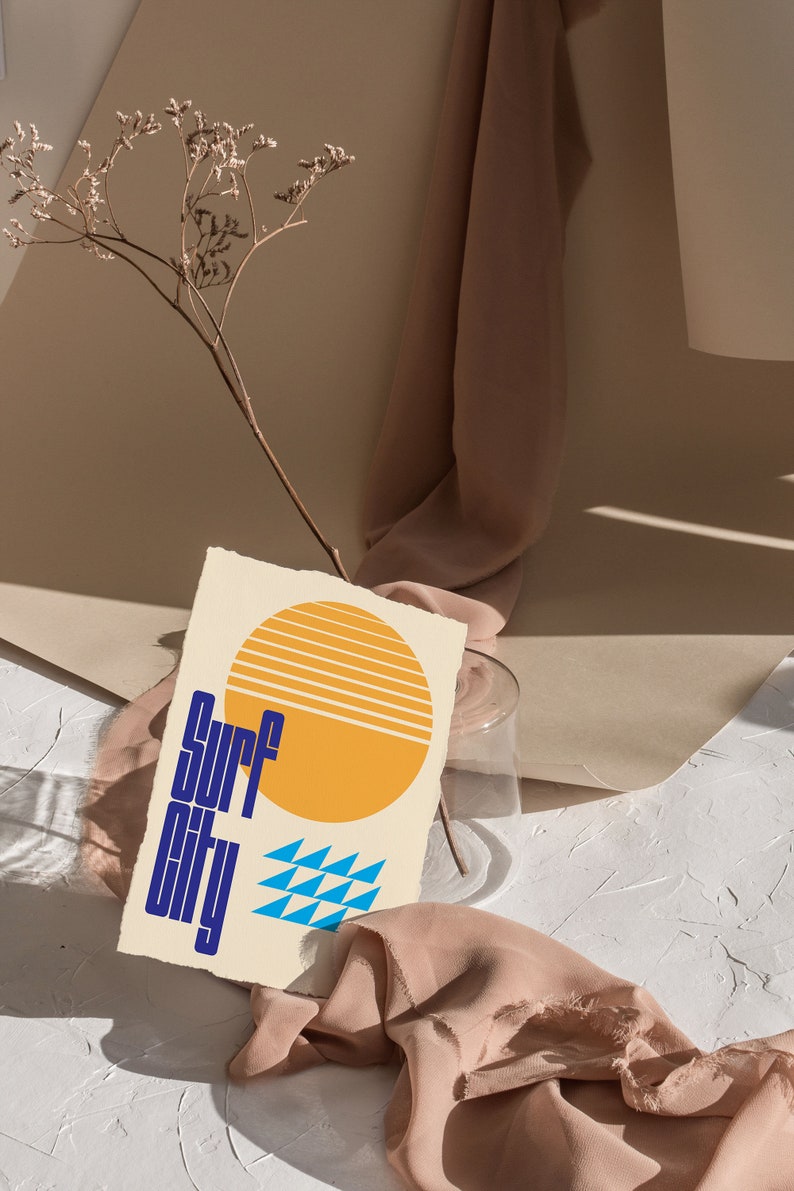 Puede incluir: Un fondo texturizado beige y blanco con una tela marr&oacute;n drapeada sobre una superficie blanca. Un sol amarillo con rayas naranjas y un patr&oacute;n geom&eacute;trico azul y blanco est&aacute;n en una tarjeta crema con el texto "Surf City" en azul.