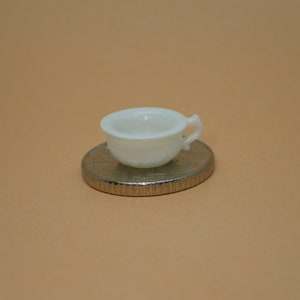 May include: A white ceramic chamber pot with a handle, sitting on a silver coin.