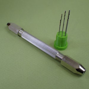 May include: A silver hand drill with a green plastic case containing six drill bits.