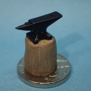 May include: A miniature black metal anvil on a wooden base, with a silver coin in the background.