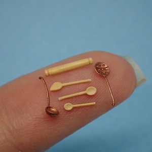 Puede incluir: Un juego de utensilios de cocina en miniatura, que incluye un rodillo, una cuchara para servir, una cuchara ranurada y dos cucharas de madera. Los utensilios están hechos de madera y metal y están pintados en tonos marrones y cobre.