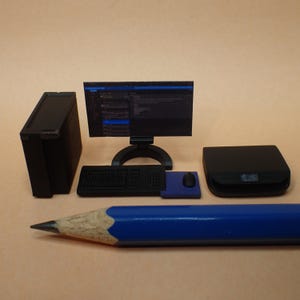 Könnte beinhalten: Ein schwarzes Miniatur-Computerset mit einem Monitor, der Code anzeigt, einer Tastatur, einer Maus und einem Tower. Das Set befindet sich auf einer braunen Oberfläche mit einem blauen Bleistift.