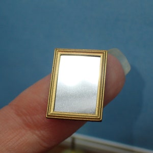 May include: A small, gold-framed mirror with a reflective surface. The mirror is held in a hand.