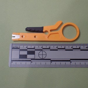 May include: Orange and black wire stripper tool with a small blade and a circular handle. The tool is measured against a ruler.