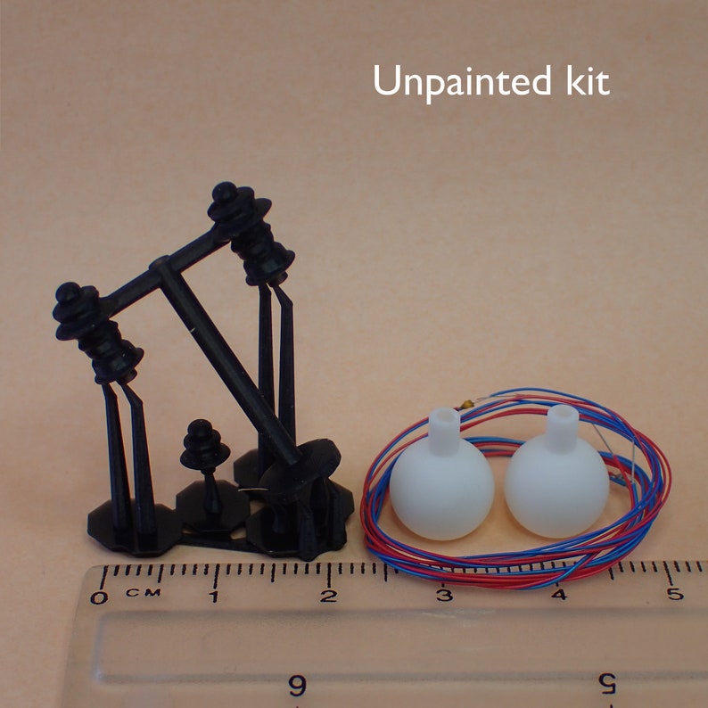 May include: Unpainted kit of a black metal model train crossing gate with two white plastic light bulbs and red and blue wires.