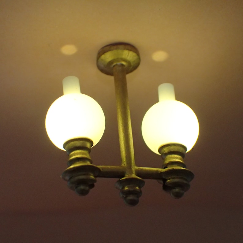 May include: A gold-toned chandelier with two frosted glass globes. The globes are lit and emit a warm glow.